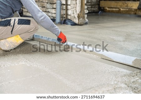 A construction worker skillfully smooths fresh concrete with a straightedge, creating a level surface. This image captures the essence of skilled labor and home renovation.