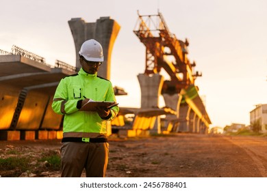 A construction worker is standing on a bridge, talking on his cell phone. The scene is set in a construction site, with a large crane in the background. The worker is wearing a yellow jacket