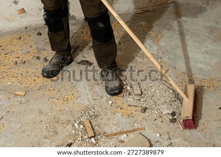 Construction worker sweeping debris on a concrete floor during renovation cleanup. Concept of manual labor, workplace safety, industrial cleaning and post-construction maintenance
