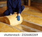 Construction worker thermally insulating house attic with glass wool 