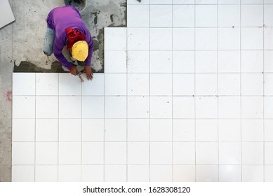 Construction worker tiler is tiling, Ceramic tile floor adhesive at factory building.