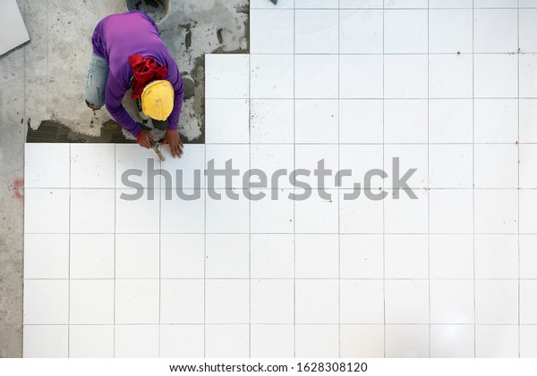 Construction worker tiler is tiling, Ceramic\
tile floor adhesive at factory\
building.