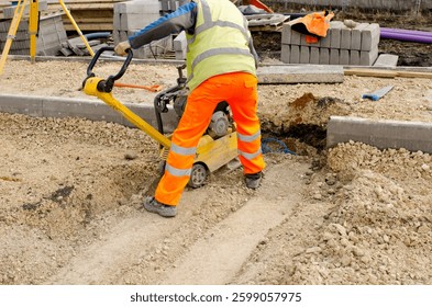 Construction worker uses compactor to compress gravel at a building site