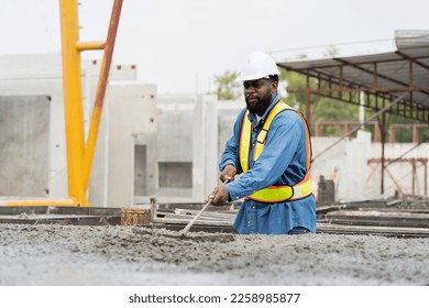 Construction worker uses long steel trowel spreading wet concrete pouring at precast concrete wall construction site. Worker or mason working or making smooth surface of concrete with equipment tool