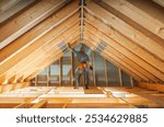 A construction worker uses a measuring tape to check the dimensions of roof trusses in a newly built attic, surrounded by wooden beams and bright daylight.