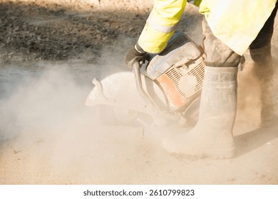 Construction worker uses petrol saw to cut through concrete creating cloud of dust