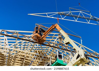 Construction Worker Using Air Hammer Nailing Beams Of Wooden Frame Roof Rafters In His Domestic Building With Wooden Framework Beams