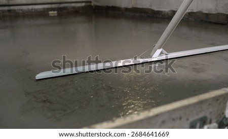 Construction worker is using a bull float to level a freshly poured concrete slab.