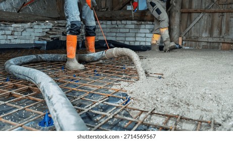 Construction worker using concrete pump to pour concrete slab for foundation. Reinforcement mesh is visible, showcasing active building site and construction activity.