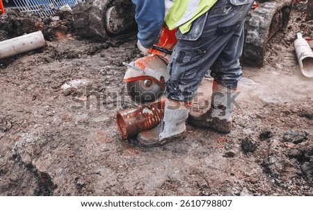 Construction worker using concrete saw to cut through drainage pipe