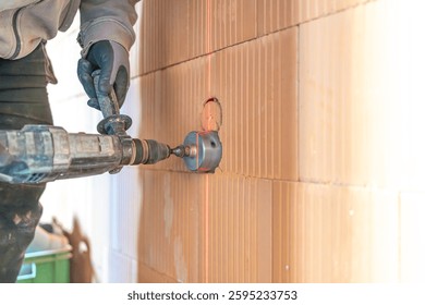 Construction worker using core drill and laser level on brick wall