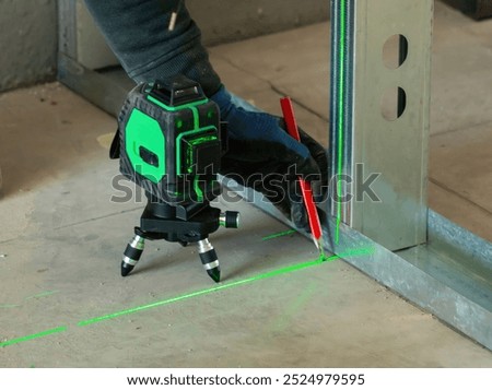Construction worker using a cross line laser level and marking a red line on a concrete floor