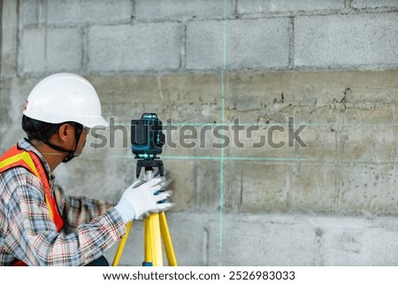 Construction worker is using cross-line laser level meter with line green beam to mark the floor in construction site. Tools for measuring distances.