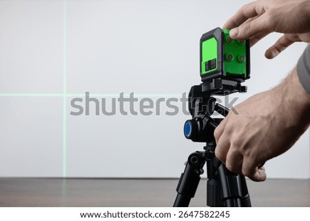 Construction worker is using cross-line laser level meter with line green beam to mark the floor in construction site.