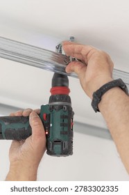 Construction worker using drill on metal profile frame for drywall suspended ceiling system near air duct and gypsum board panels. Installation process in an apartment under renovation