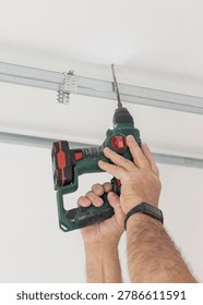 Construction worker using drill on metal profile frame for drywall suspended ceiling system near air duct and gypsum board panels. Installation process in an apartment under renovation