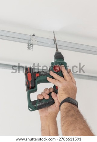 Construction worker using drill on metal profile frame for drywall suspended ceiling system near air duct and gypsum board panels. Installation process in an apartment under renovation