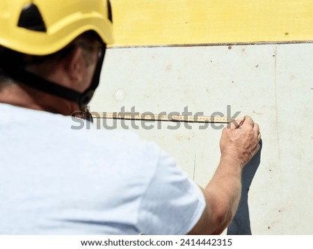 Construction worker using folding ruler and pencil on concrete wall