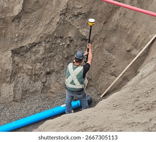 Construction worker using a GPS receiver to record as-built data for a newly installed water main pipe during underground utility work.
