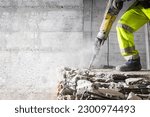 Construction worker using heavy-duty jackhammer tool and breaking reinforced concrete. Demolishing building interior. Under construction.