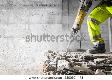 Construction worker using heavy-duty jackhammer tool and breaking reinforced concrete. Demolishing building interior. Under construction.