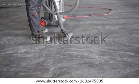 Construction worker is using industrial vacuum cleaner to remove dust and debris after laying floor tiles in a new building