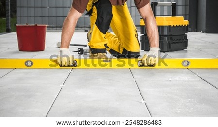 A construction worker is using a level tool to ensure tile alignment on a floor at a construction site. The worker is focused and dressed for the task.