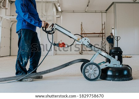Construction worker using machine polishing surface floor smoothing and finishing hardener or epoxy concrete in the factory.