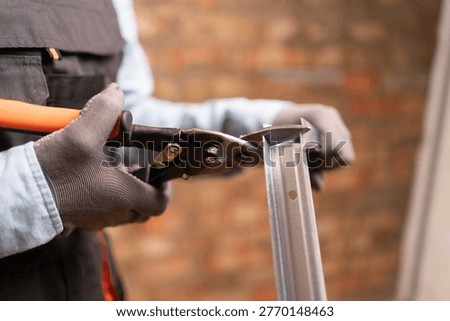 Construction worker using metal shears snips cut of galvanized steel from drywall profile. close-up