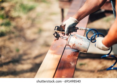 Construction worker using paint gun and brown paint during renovation works. Painting fence