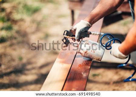 Construction worker using paint gun and brown paint during renovation works. Painting fence