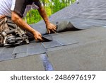 Construction worker using pneumatic nail gun to install new bitumen shingles on roof