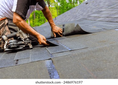 Construction worker using pneumatic nail gun to install new bitumen shingles on roof