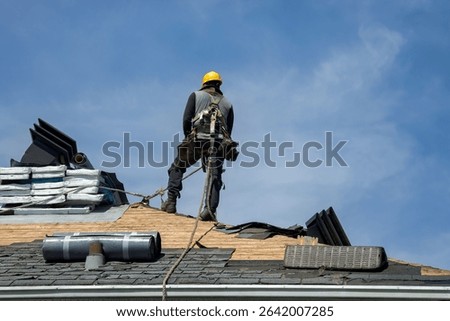 Construction worker using pneumatic nailer and safety helmet applying roofing materials against blue sky backdrop