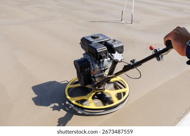 Construction worker using power trowel on concrete surface, Close-up of a construction worker operating a power trowel machine to smooth and finish freshly poured concrete on a building site.