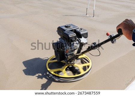 Construction worker using power trowel on concrete surface, Close-up of a construction worker operating a power trowel machine to smooth and finish freshly poured concrete on a building site.