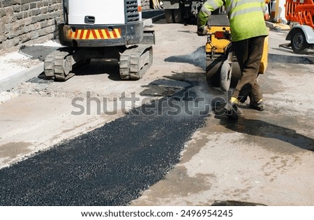 Worker compacts tarmac using vibration plate compactor