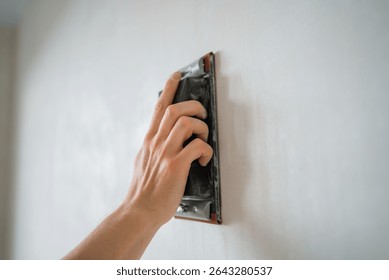 Construction worker is using sandpaper for smoothing wall surface, preparing it for painting or wallpapering, ensuring a perfect finish during home renovation