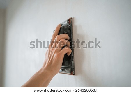 Construction worker is using sandpaper for smoothing wall surface, preparing it for painting or wallpapering, ensuring a perfect finish during home renovation