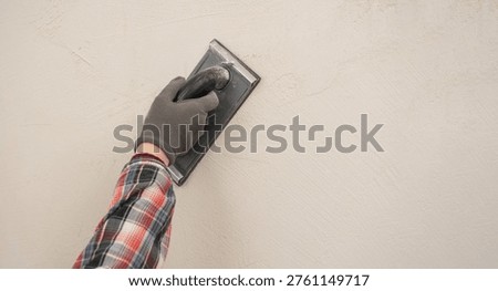 Construction worker using sandpaper for smoothing wall surface, finish during home renovation. close-up