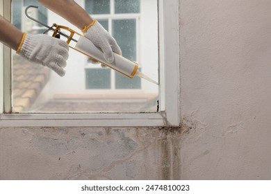 Construction worker using silicone sealant caulk for repair leaked inside window frame.