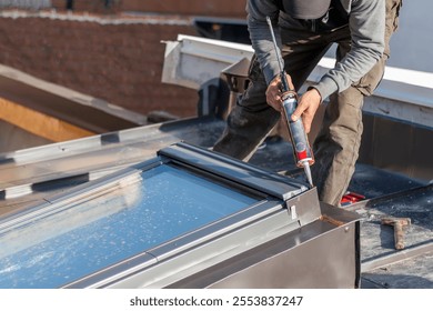 Construction worker using silicone sealant adhesive to fix a metal sheet on the skylight window. A roofer and window master work. 