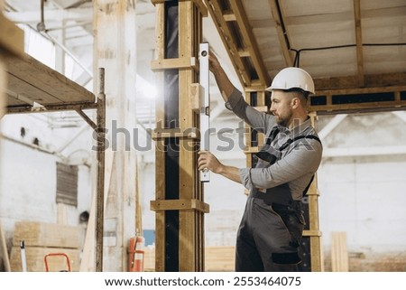 Construction worker using spirit level ensuring vertical alignment of support beam during modular building construction