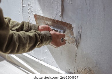 Construction worker is using a trowel to apply plaster on a wall, smoothing the surface and preparing it for painting or wallpapering during a home renovation project
