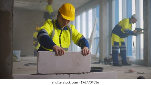 Construction Worker Using Trowel And Tools For Building Wall With Bricks And Mortar. Professional Builder Installing Brick Wall In Renovating House Or Office.