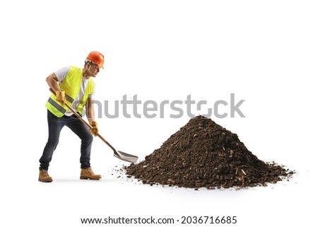 Construction worker with a vest and hardhat digging earth with a shovel isolated on white background
