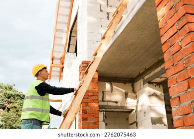 Construction worker at wall, checks alignment, starts building process, measures height, bricklayer, team task, installation preparation, technical check.