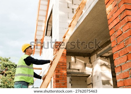 Construction worker at wall, checks alignment, starts building process, measures height, bricklayer, team task, installation preparation, technical check.