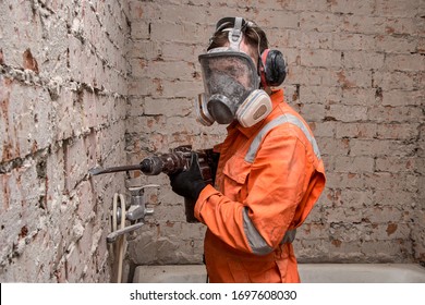 Construction  Worker Wearing Full Face Respirator Mask And Ear Defenders For Working With Hammer Drill.