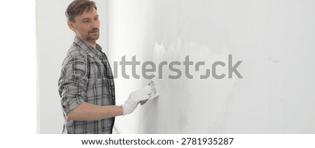 Construction worker wearing gloves and using a putty knife to plaster a white wall, performing home renovation and improvement tasks with precision